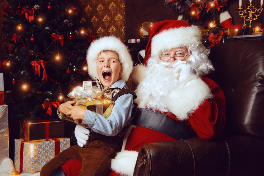 Santa Claus and shouting cute boy sitting in Christmas room with gifts. Christmas home decoration.